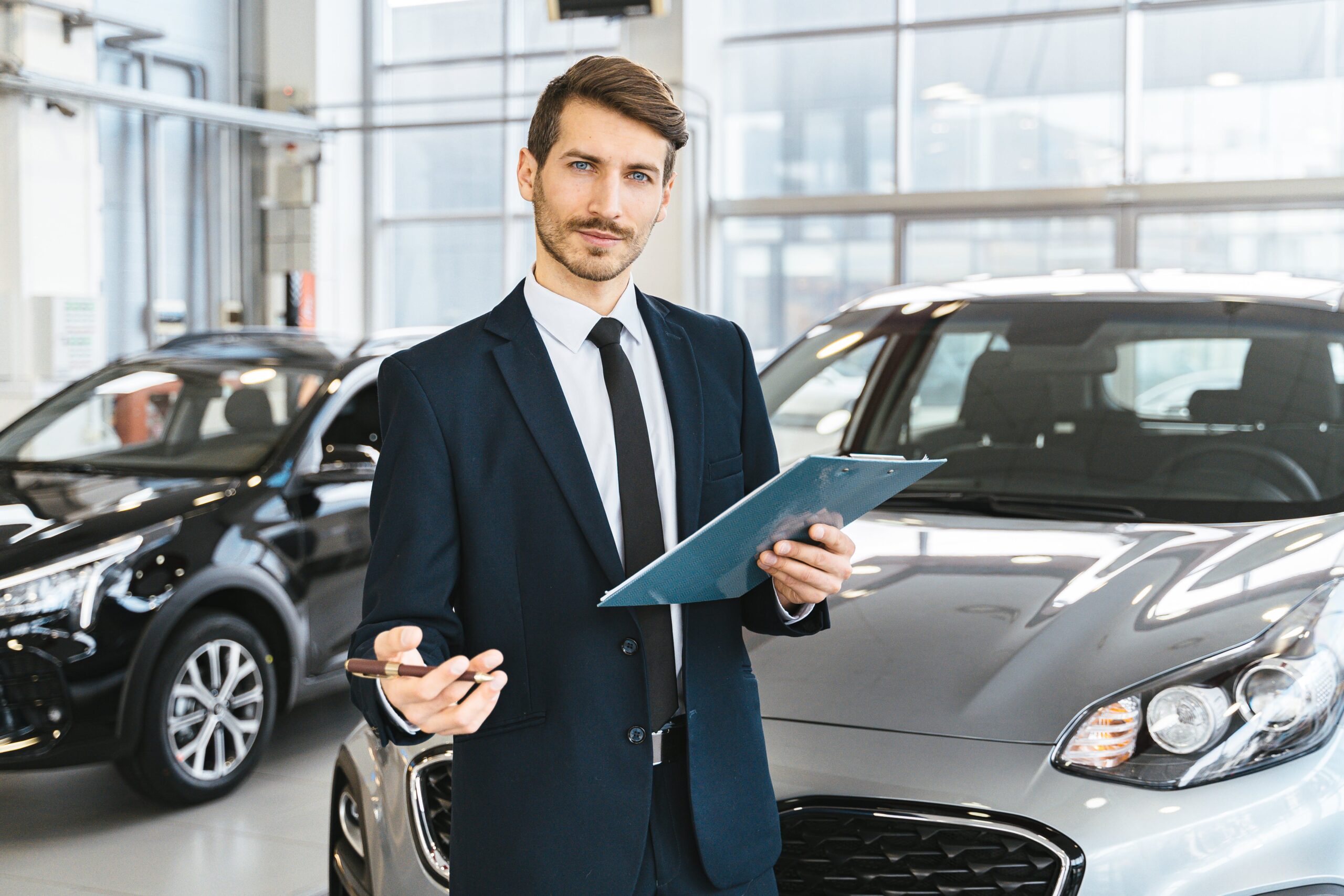 Salesman standing in front of 2 vehicles in a car dealership's showroom.