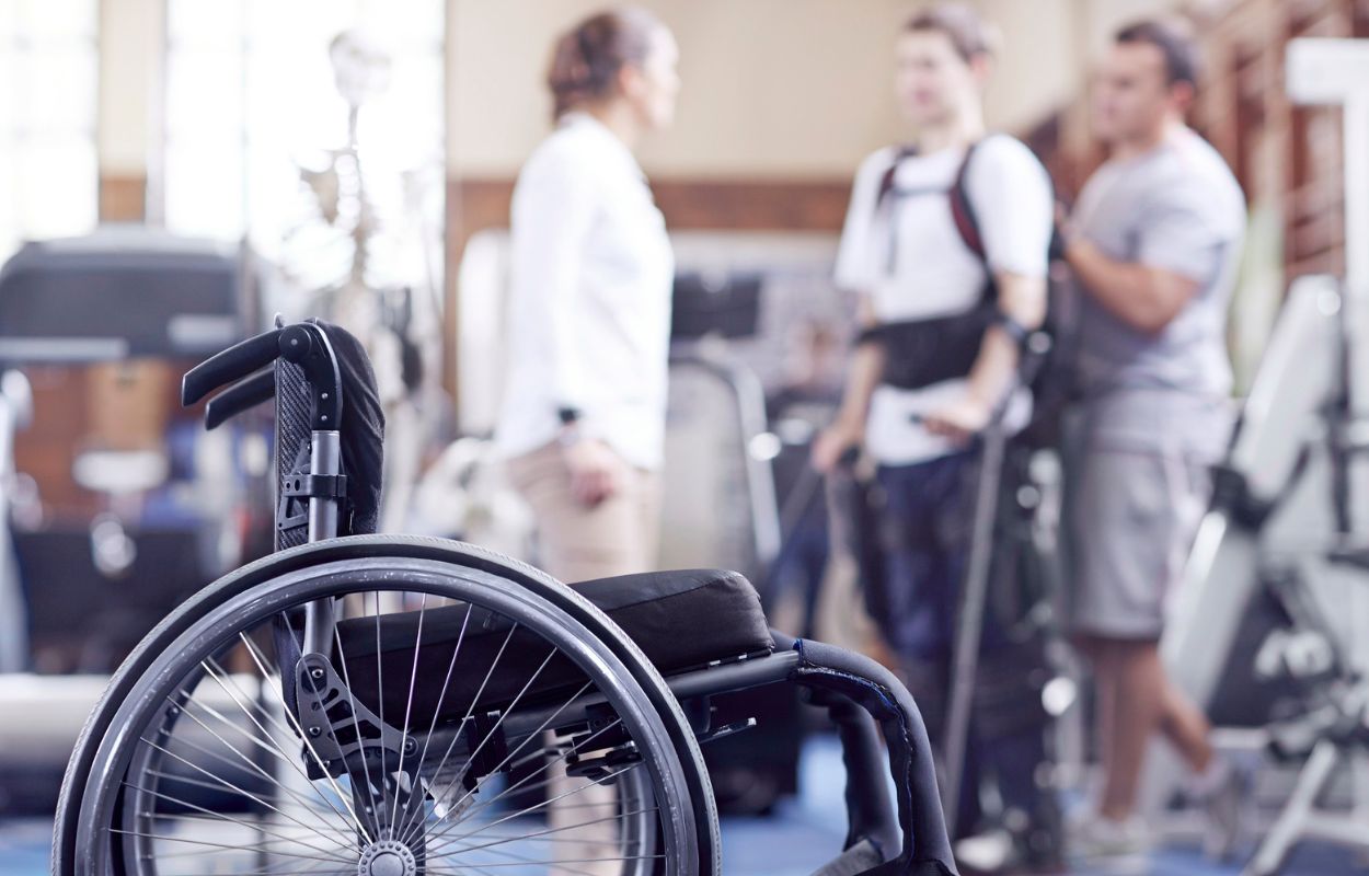 Wheelchair in foreground of image, with physical therapy patient seen in background.
